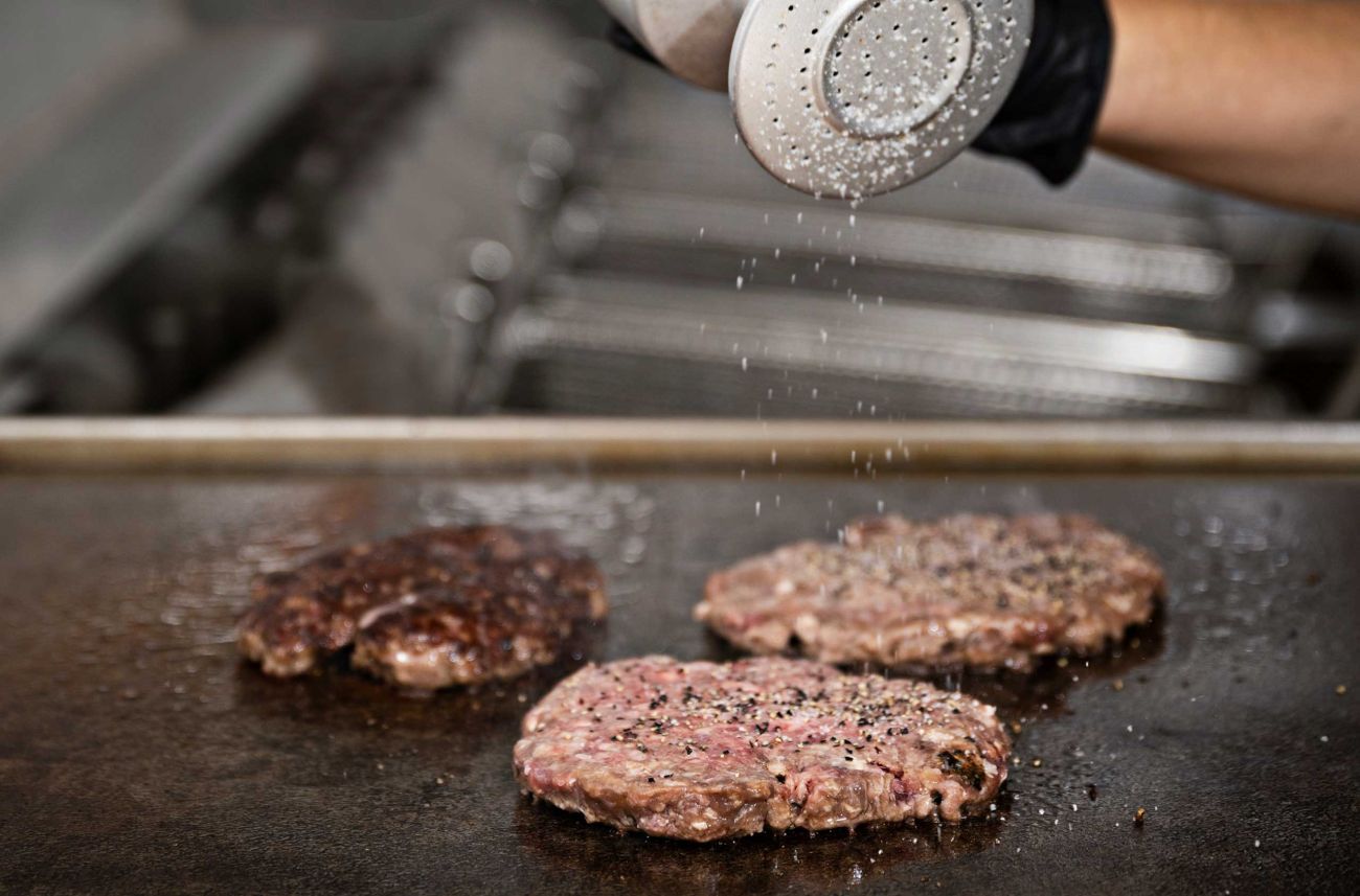 Frisches Burgerpatty wird auf dem Grill gewürzt