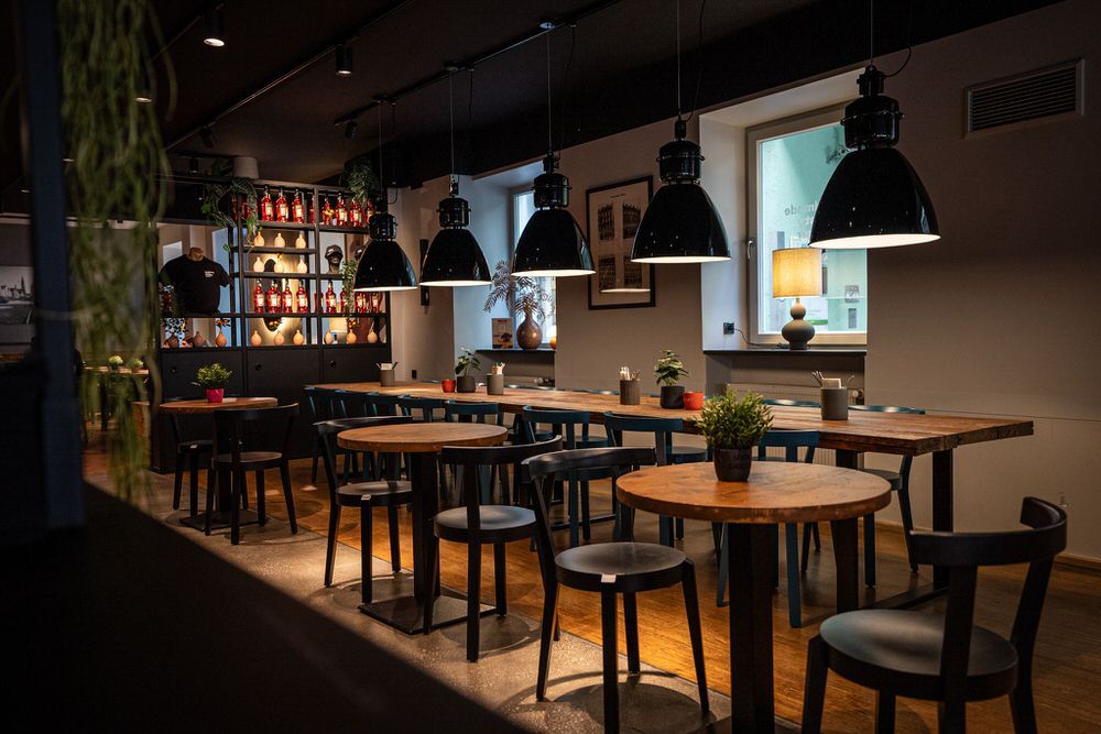 Innenansicht von "Ruff's Burger" mit Holztischen, schwarzen Stühlen, großen Hängelampen und beleuchtetem Regal im Hintergrund.