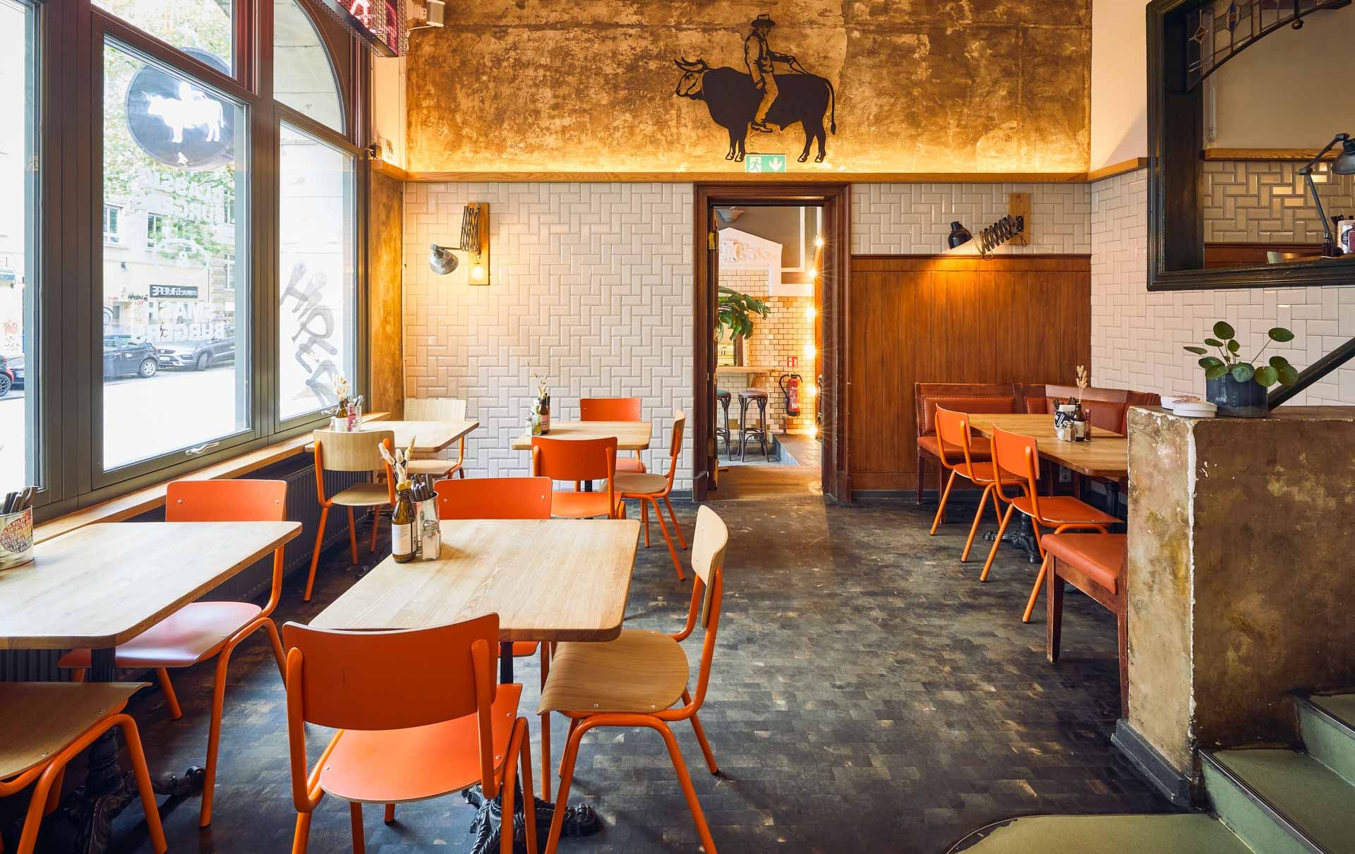 Barbereich von "Ruff's Burger" mit Holztheke, Metallverkleidung, Neon-WC-Schriftzug im Hintergrund und gelbem Gläserregal.