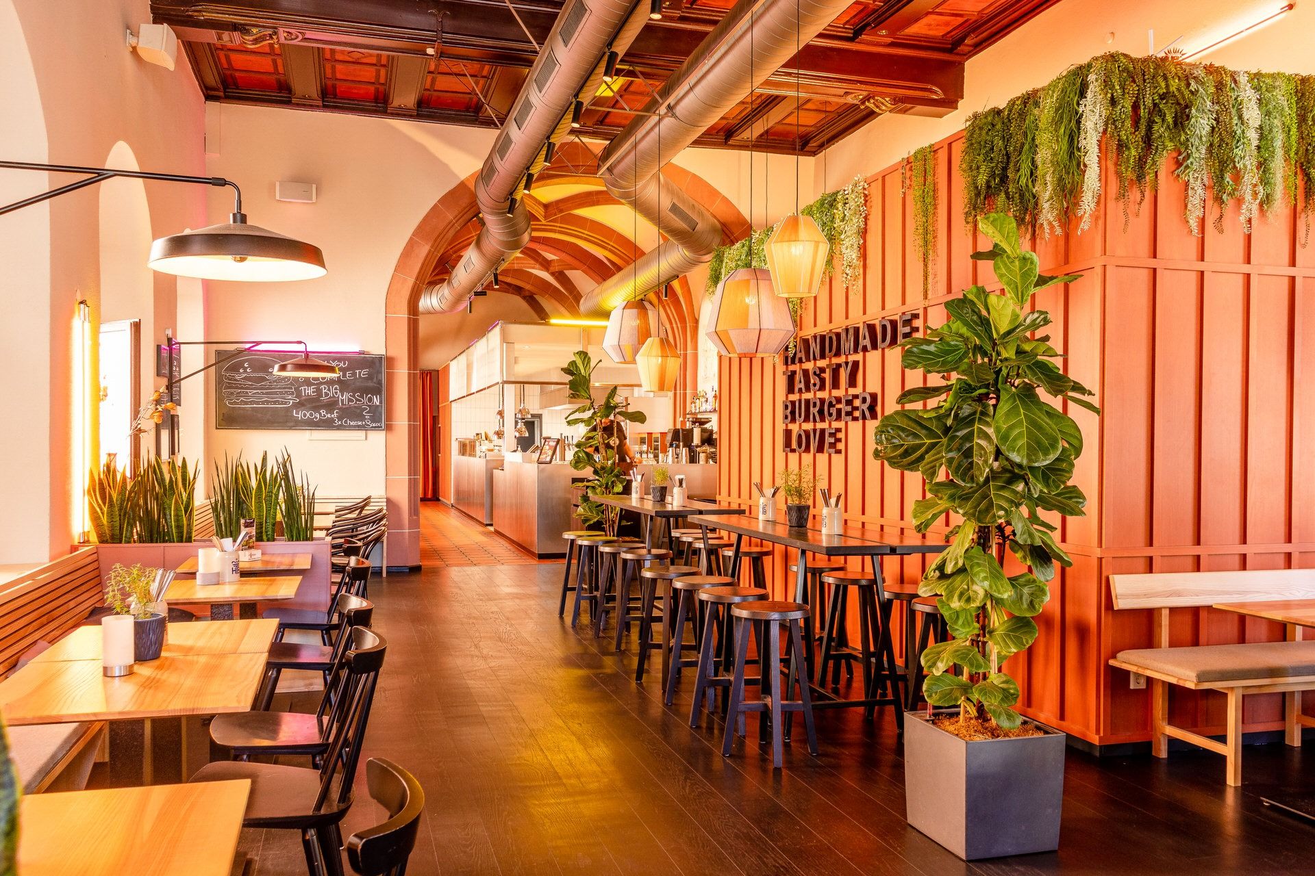 Innenansicht von "Ruff's Burger" mit Holztischen, Hochstühlen, Pflanzen, hölzerne Wandverkleidung mit dem Schriftzug "Handmade Tasty Burger Love".