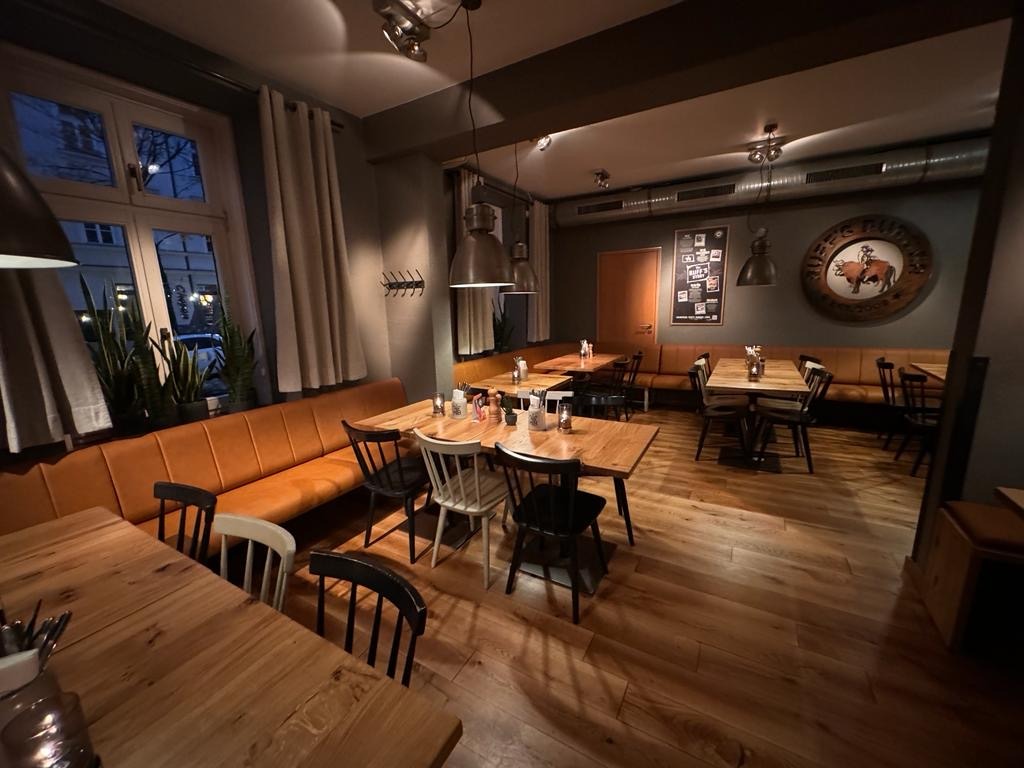 Innenansicht von "Ruff's Burger" mit Holztischen, schwarzen und weißen Stühlen, Polsterbänken, Wandlogo und Hängelampen.