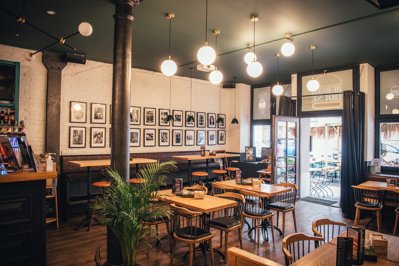 Innenbereich von "Burger House" mit Holztischen, Stühlen, weißer Backsteinwand und großflächiger Schwarzweiß-Fotogalerie.