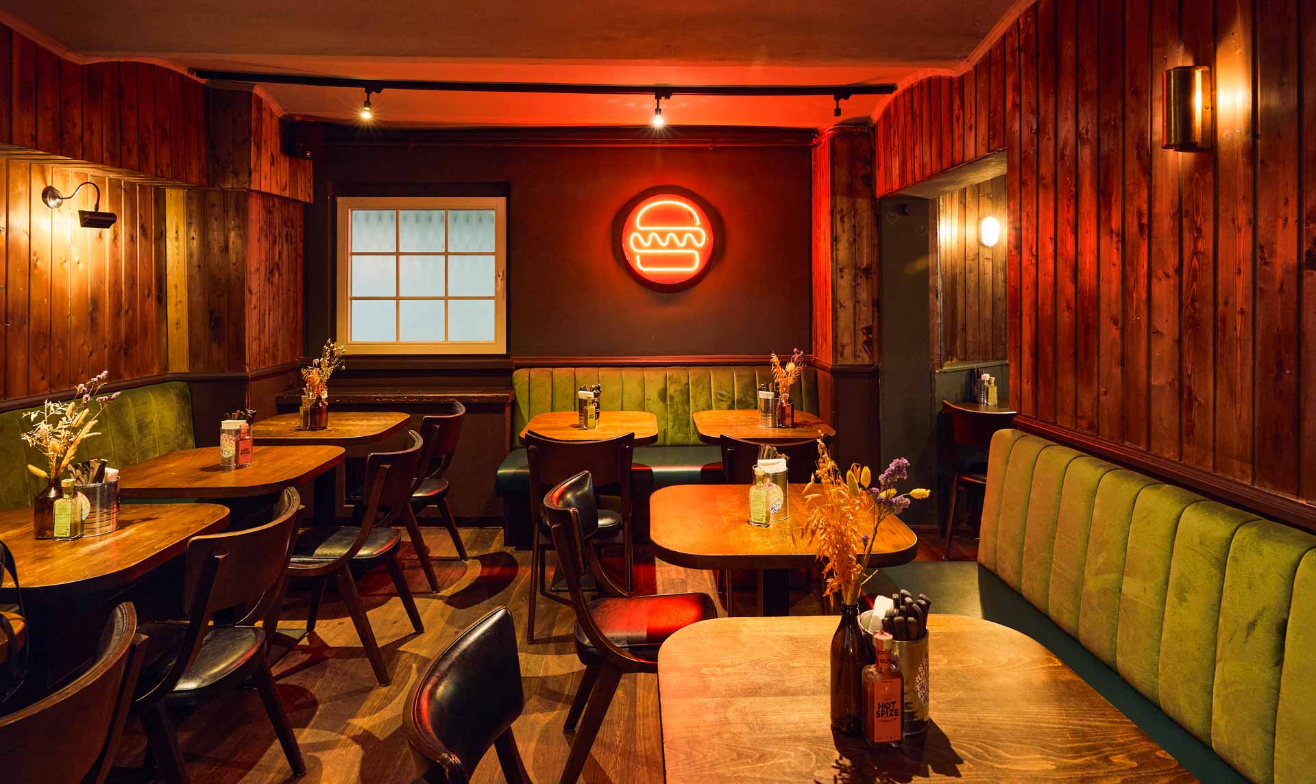 Innenansicht von "Otto's Burger" mit mehreren grünen Polsterbänken, Holztischen, Stühlen und vertäfelter Holzverkleidung.
