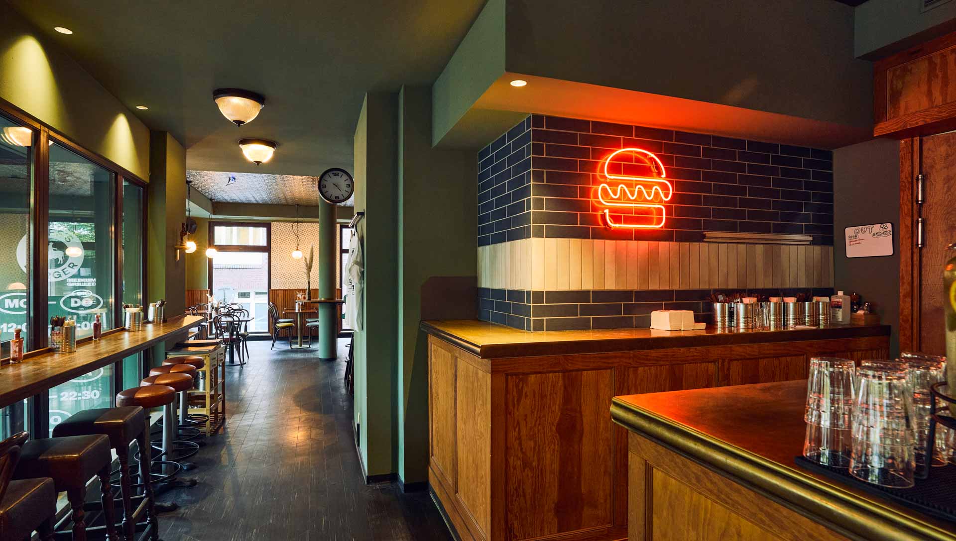 Barbereich von "Otto's Burger" mit Holztheke, offenen Regalen, Hängelampen, Fliesenwand und dekorativer Decke.