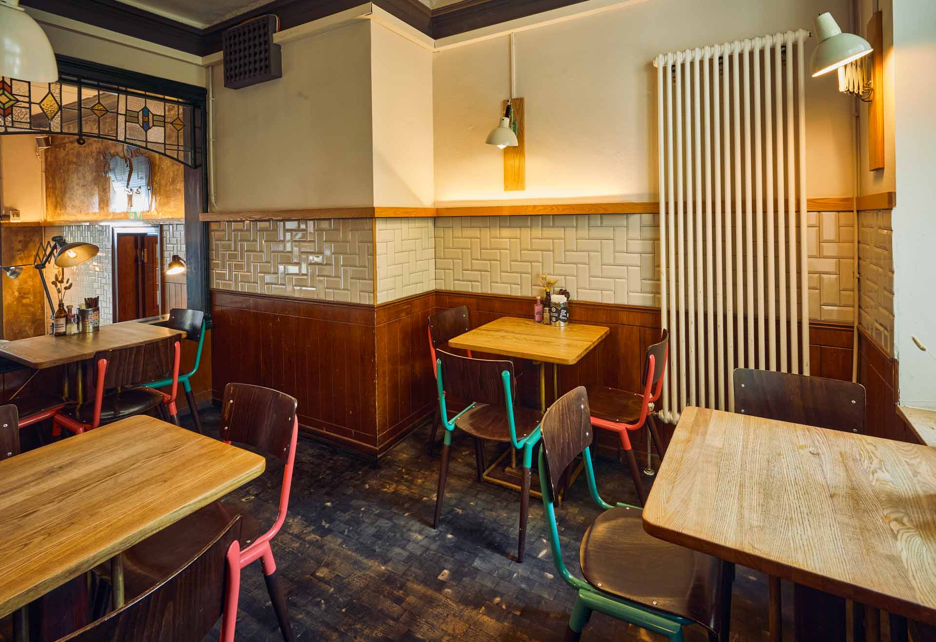 Barbereich von "Ruff's Burger" mit Holztheke, Metallverkleidung, Neon-WC-Schriftzug im Hintergrund und gelbem Gläserregal.